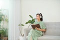 Mage of focused asian woman using headphones and writing down notes while sitting on sofa at home