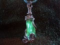 Magic necklace with a green glowing crystal gemstone wrapped with copper.