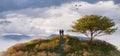 Magical fantasy scene with man and woman couple on top of hill and mountain landscape in background