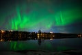 A magical illuminated view of aurora borealis with a city scape under starry clear sky and reflection from lake water in Royalty Free Stock Photo