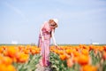 Beautiful young long red hair woman wearing in striped dress and straw hat standing on colorful flower tulip field in Holland Royalty Free Stock Photo