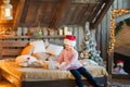 A magical photo of a little girl at home on the bed under Christmas. A girl in a pink sweater unwraps a New Year`s gift in a bedro