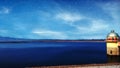 A magical starry night on the lake bank with lighthouse in the blue cloudy sky.