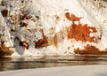 Magical sunny winter day, landscape with red sandstone cliffs that are snowy with snow, frozen icicles on the cliff wall