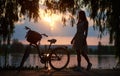 Magical sunset landscape. Silhouette of woman in dress and retro bicycle with basket against lake. Royalty Free Stock Photo