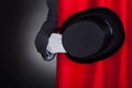 Magician holding hat behind stage curtain