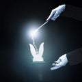 Magician performing trick with magic wand against black glowing background . High quality and resolution beautiful photo concept Royalty Free Stock Photo