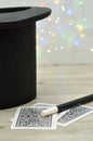 A magicians hat, wand and cards against an out of focus light background