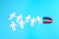 Magnet attracting paper cutouts of humans on light blue background Royalty Free Stock Photo