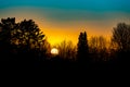 Magnificent evening sky with orange sun ball at sunset behind bare trees. Royalty Free Stock Photo