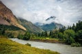 Magnificent mountain landscape - fog on top of hills, a curve river, green trees and grass on the shore. Natural beauty of Altai