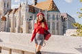 Magnificent slim girl in trendy attire standing in front of beautiful palace in sunny september day. Emotional curly