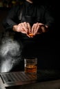 magnificent view of hands of bartender spraying oils from an orange peel on cocktail on dark background.