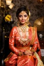 Magnificent young Indian bride in luxurious bridal costume with makeup and heavy jewellery is sitting in a chair in with classic