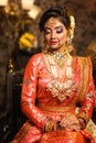 Magnificent young Indian bride in luxurious bridal costume with makeup and heavy jewellery is sitting in a chair Royalty Free Stock Photo