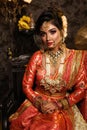 Magnificent young Indian bride in luxurious bridal costume with makeup and heavy jewellery sitting in a chair with classic vintage Royalty Free Stock Photo