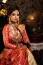 Magnificent young Indian bride in luxurious bridal costume with makeup and heavy jewellery sitting in a chair with classic vintage Royalty Free Stock Photo