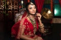 Magnificent young Indian bride in luxurious dress and precious jewellery is sitting in a chair in a luxury apartment. Classic Royalty Free Stock Photo