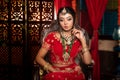Magnificent young Indian bride in luxurious dress and precious jewellery is sitting in a chair in a luxury apartment. Classic Royalty Free Stock Photo