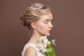 Magnificent young woman with bridal hairstyle and white tulip flowers on brown background