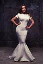 Magnificent young woman in a white fishtail maxi dress over black worn background