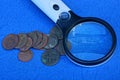 Magnifier and a bunch of old copper coins on a blue table Royalty Free Stock Photo