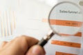 Magnifier on a coloured funnel chart printed on a white sheet of paper during a business meeting