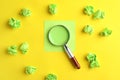 Magnifier glass, empty card and green crumpled paper sheets on yellow background. Find keywords concept