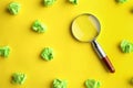 Magnifier glass and green crumpled paper sheets on yellow background. Find keywords concept