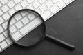 Magnifier glass and keyboard on black slate background. Find keywords concept Royalty Free Stock Photo