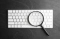 Magnifier glass and keyboard on black background, flat lay. Find keywords concept Royalty Free Stock Photo