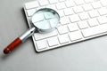 Magnifier glass and keyboard on grey stone background, closeup. Find keywords concept Royalty Free Stock Photo