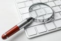 Magnifier glass and keyboard on white table, closeup. Find keywords concept Royalty Free Stock Photo