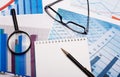Magnifier, glasses, white notebook and pen on bright diagrams. Workplace close up Royalty Free Stock Photo