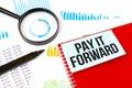 Magnifier,marker and red notebook with white card. Text PAY IT FORWARD. Financial concept Royalty Free Stock Photo