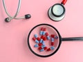 Magnifier with medical pills and red stethoscope closeup