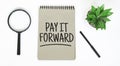 A magnifying glass, a blank brown notebook on a white table. PAY IT FORWARD sign Royalty Free Stock Photo