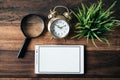 Magnifying glass, clock, green plant and digital tablet with blank screen on wooden table background Royalty Free Stock Photo