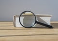 Magnifying glass with close thick book on wood table with day light