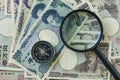 Magnifying glass and compass on pile of japanese yen banknotes a