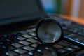 Magnifying glass on dusty dirty laptop keyboard in a dark room