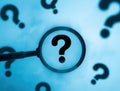 A magnifying glass focusing on a central question mark surrounded by other out-of-focus question marks Royalty Free Stock Photo