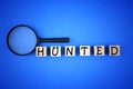 Magnifying glass with HUNTED wording on wooden block on blue background Royalty Free Stock Photo