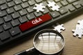 Magnifying glass, jigsaw puzzle and computer keyboard with red button written with QNA or Questions and Answers Royalty Free Stock Photo