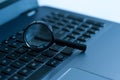 Magnifying glass on laptop keyboard on blue tone Royalty Free Stock Photo