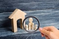 Magnifying glass is looking at the Big family is standing near the house. Wooden figures of persons stand near a wooden house. Royalty Free Stock Photo