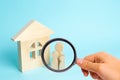 Magnifying glass is looking at the Family is standing near the house. Wooden figures of persons stand near a wooden house. Royalty Free Stock Photo