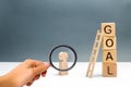 Magnifying glass is looking at the figure of a man stands near a tower of cubes with the word goal. achieving the goal, dedication