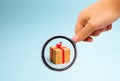 Magnifying glass is looking at the Gift box on blue background. Minimalism. The approach of the New Year holidays or birthday. Royalty Free Stock Photo