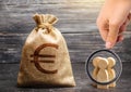 Magnifying glass is looking at a money bag with a euro sign and people figurines. evaluation of the cost of the work